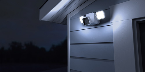 The Blink Outdoor + Floodlight mounted on a wall with the LED floodlight on.
